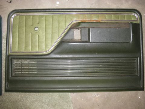 1979 Ford Bronco - A dark green driver's side door panel with a green upholstered section and a horizontal ribbed speaker grille is shown laid flat on a concr…