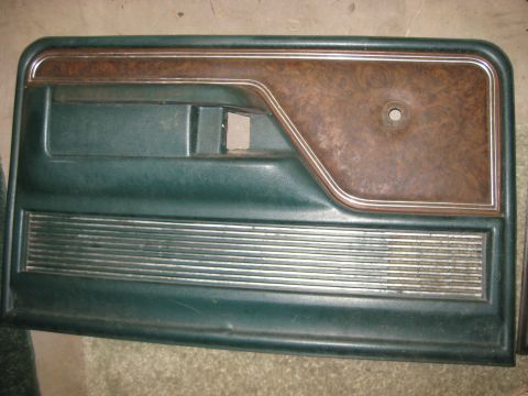 1979 Ford Bronco - A dark green interior door panel with wood grain trim and horizontal chrome accents is shown laid flat on a concrete floor.