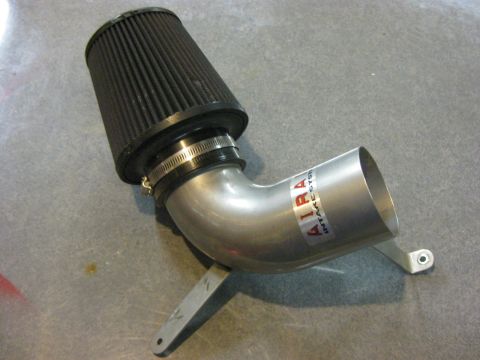 1979 Ford Bronco - A silver metal intake tube with a black cone air filter is shown mounted on a gray textured surface. A red and white sticker with the text…
