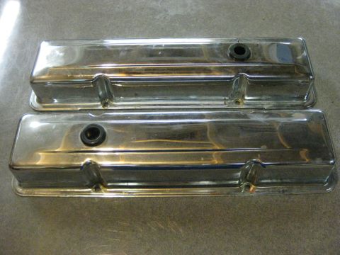 1979 Ford Bronco - Two chrome valve covers are shown from a top-down perspective, resting on a textured gray surface. Each valve cover has a black rubber grom…