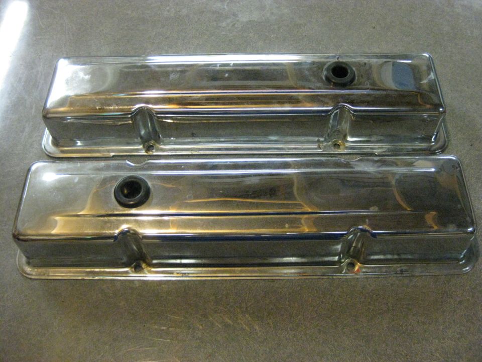 Two chrome valve covers with black grommets on a gray surface.