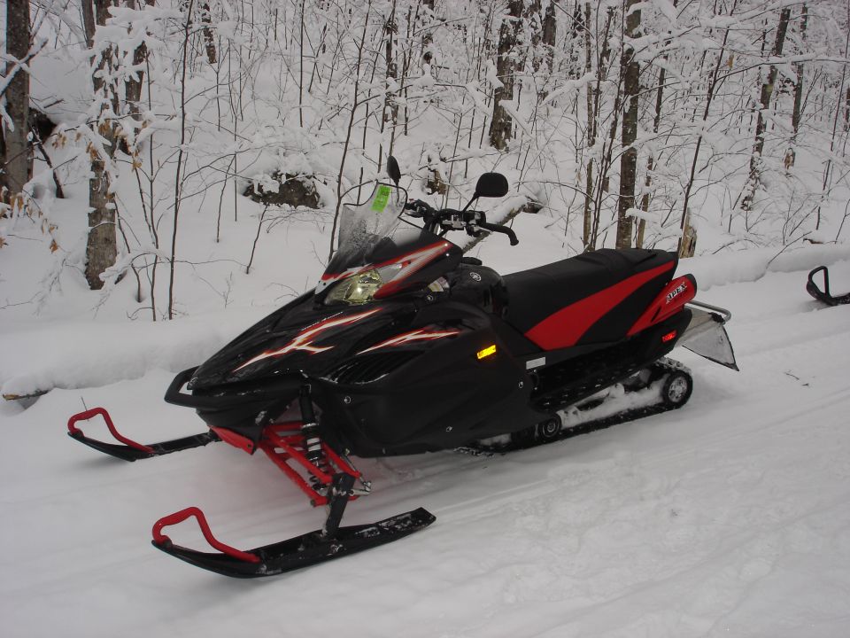 Black and red Yamaha Apex snowmobile parked on a snowy trail in the woods