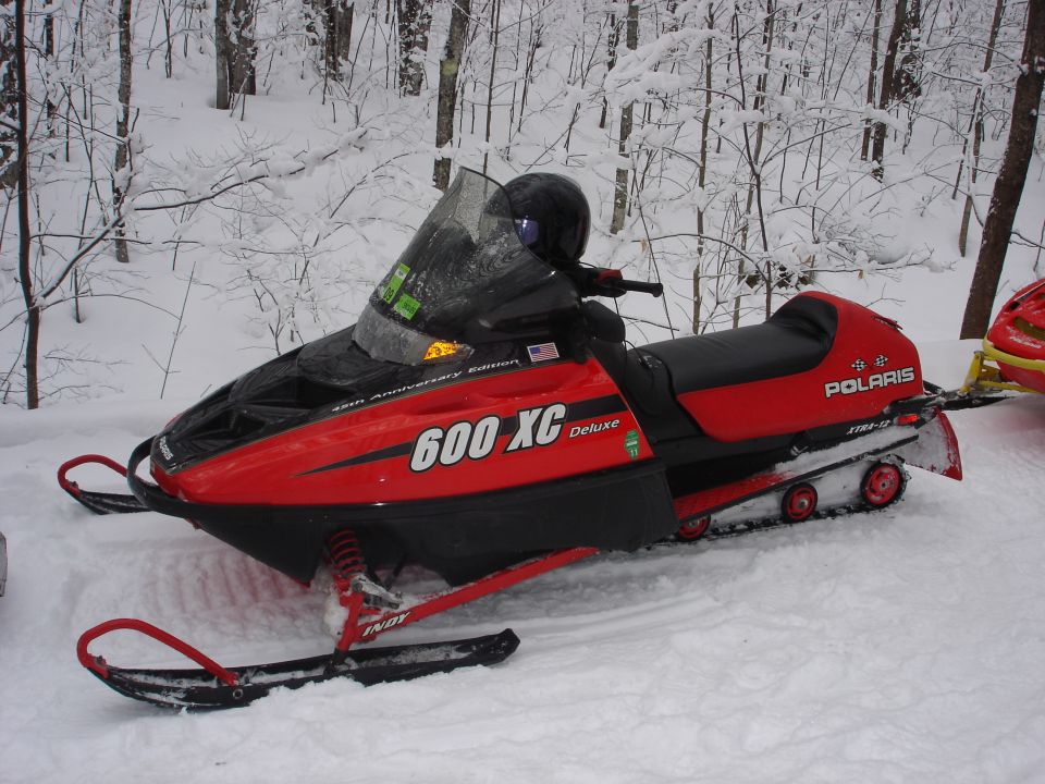 Red Polaris 600 XC Deluxe snowmobile in a snowy forest.