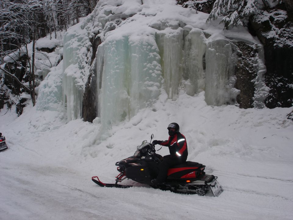 Person on a black and red snowmobile in a snowy landscape with ice formations.