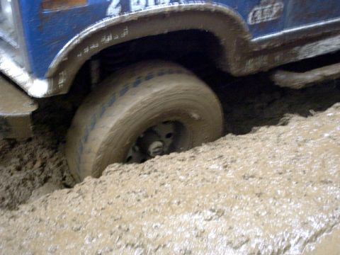 1995 Ford Bronco - A blue off-road vehicle is stuck in thick mud, with its tire submerged.