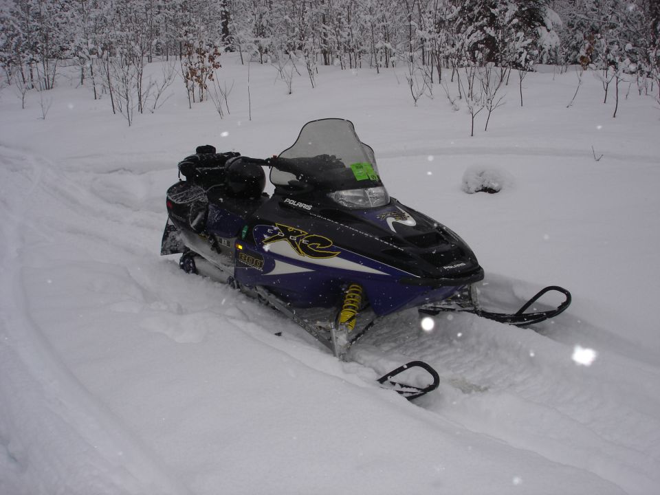 Purple and black Polaris XC snowmobile parked in deep snow, 3/4 front view