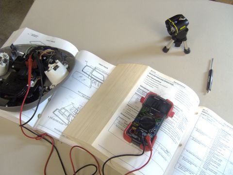 2007 Ford Mustang - Photograph of an overhead console diagnosis scene with a multimeter and open manual, not a document page itself.