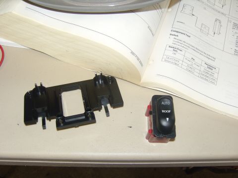 2007 Ford Mustang - Photograph of an overhead console switch bezel and an AUTO/ROOF switch next to an open service manual, not a document page itself.