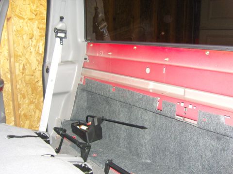 2007 Ford Mustang - Photograph of the rear interior of a red truck cab showing carpet, seat belt and the bed bulkhead, not a document.