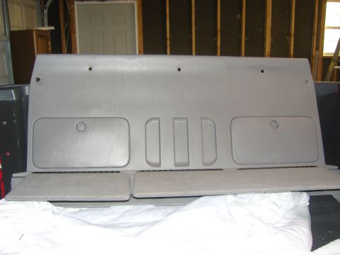 2007 Ford Mustang - Photograph of a removed gray plastic interior panel resting on white sheeting in a garage, not a document.