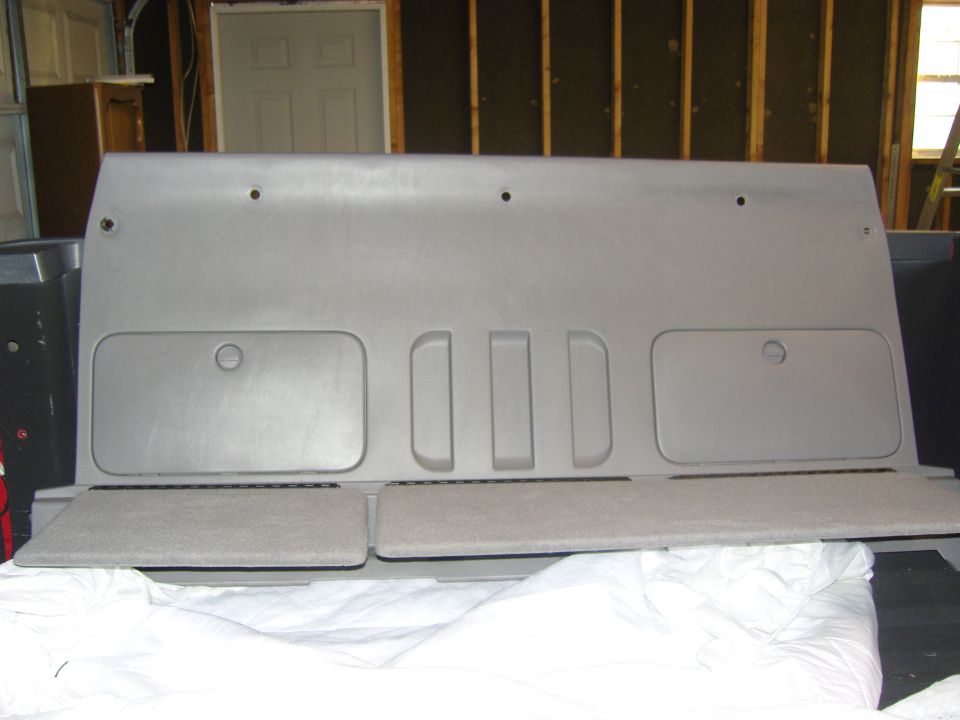 Photo of a gray rear interior trim panel laid on a garage floor
