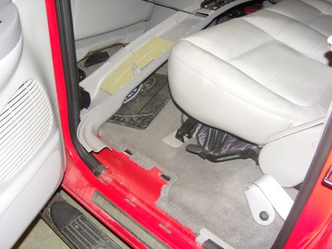 2007 Ford Mustang - Photograph of the front seat, carpeted floor and door sill area of a red truck interior, not a document.