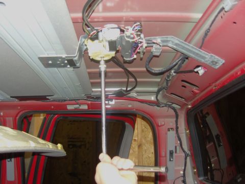 2007 Ford Mustang - Photograph of a hand servicing an overhead console motor and wiring inside a truck roof, not a document.