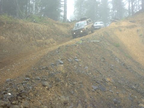 1995 Ford Bronco - Two SUVs navigate a steep, muddy incline on an off-road trail.