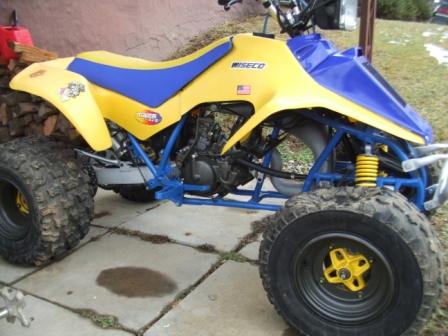 1996 Ford Bronco - A yellow and blue ATV is parked on a concrete patio next to a stack of firewood. The ATV has knobby tires and a blue frame.
