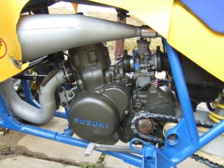 1996 Ford Bronco - Close-up view of a Suzuki two-stroke engine with a silver expansion chamber exhaust and a blue frame. The engine case has "SUZUKI" written…