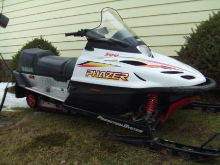1996 Ford Bronco - White and red Yamaha Phazer 500 snowmobile with windshield parked on a grassy yard next to a house wall.