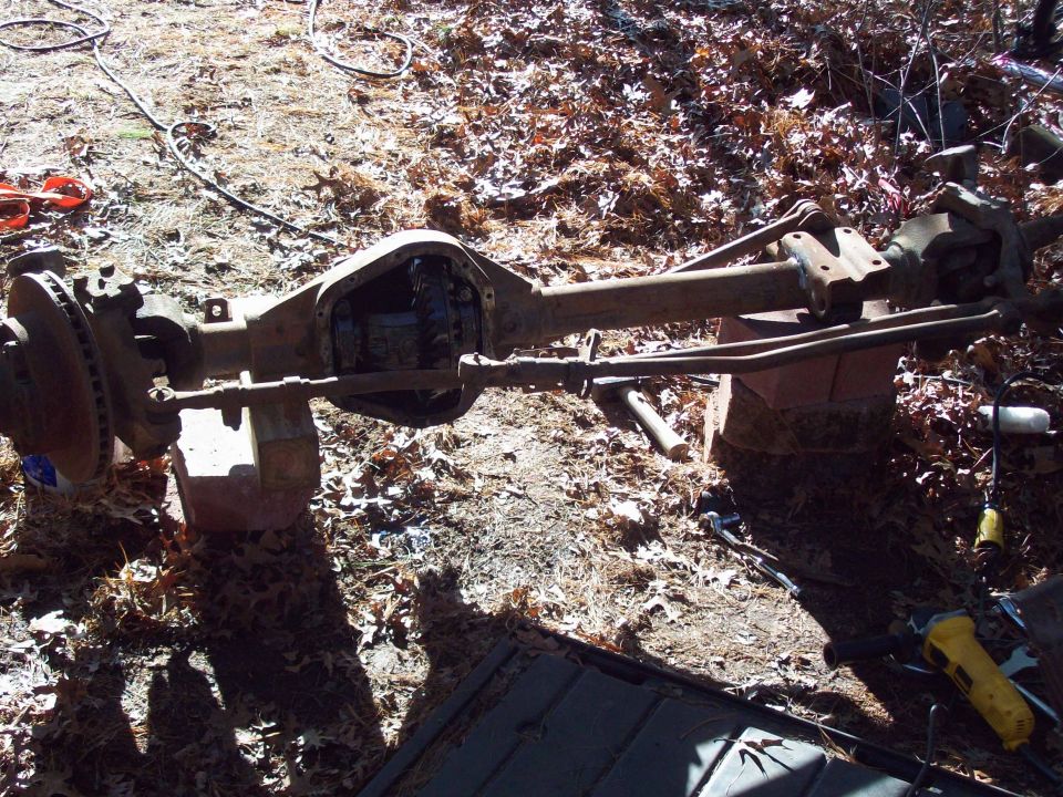 Disassembled front axle assembly with open differential housing, resting on blocks outdoors.