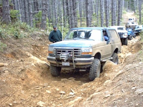 1995 Ford Bronco - A convoy of Ford Broncos navigates a challenging off-road path through a wooded area.