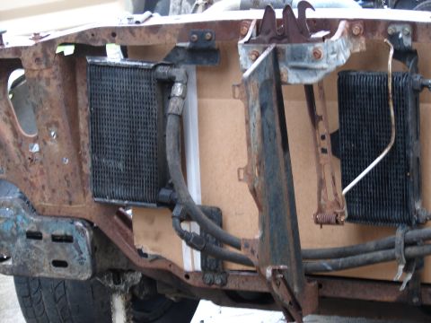 1973 Ford Ranchero - The front end of a heavily rusted vehicle chassis shows two radiators, likely for the engine and transmission, with associated hoses and mo…