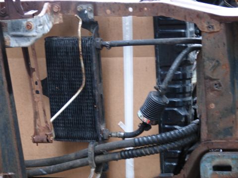 1973 Ford Ranchero - Front-end view of a stripped vehicle with the grille and bodywork removed, exposing the A/C condenser and radiator core mounted in a rusty…