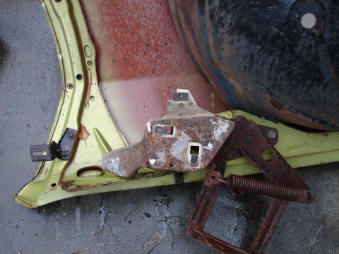 1973 Ford Ranchero - A removed hood laid upside down on wet asphalt, showing lime-green painted outer skin, surface-rusted red primer inner structure, and a bol…