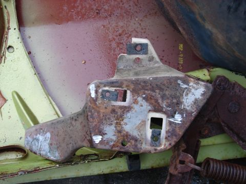 1973 Ford Ranchero - Close-up of a rusty stamped-steel body bracket or hinge-mount panel with slotted holes and captive nuts, laid over a pale green and pink pr…