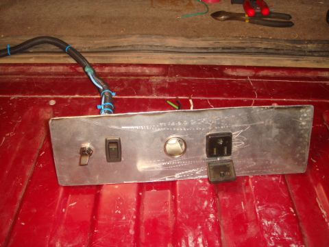 1992 Ford Bronco - A custom metal panel with a toggle switch, a rocker switch, a circular gauge, and two electrical outlets is mounted on a red surface, likel…