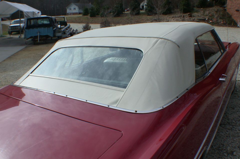 Maroon convertible with cream soft top, rear three-quarter view on gravel drive