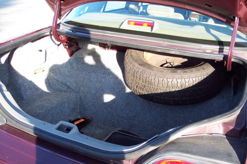 Open trunk of a dark red sedan showing spare tire and jack.