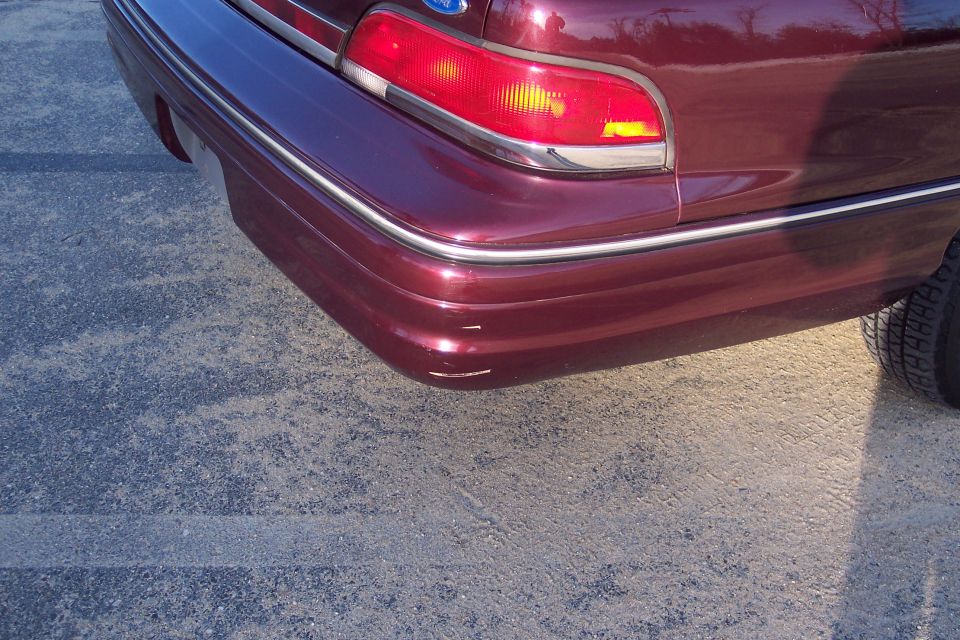 Close-up of the rear bumper and taillight of a dark red sedan.