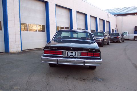 2001 Ford Crown Victoria - The rear view of a black Chevrolet Caprice sedan parked in front of a building with garage doors. The car has a chrome bumper and taillight…