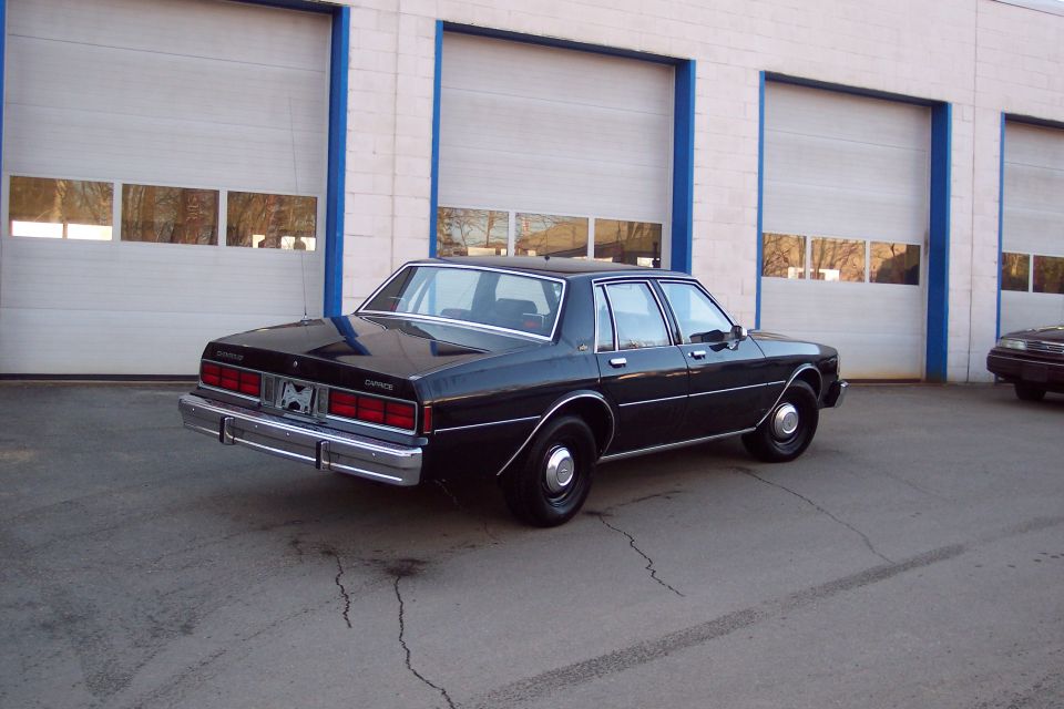 Black 1980s Chevrolet Caprice sedan parked in front of a building with garage doors.