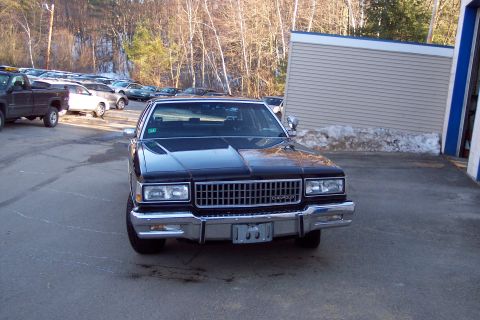 2001 Ford Crown Victoria - A black Chevrolet sedan is parked in a lot with a building and trees in the background. The car is facing the camera, showing its front gri…