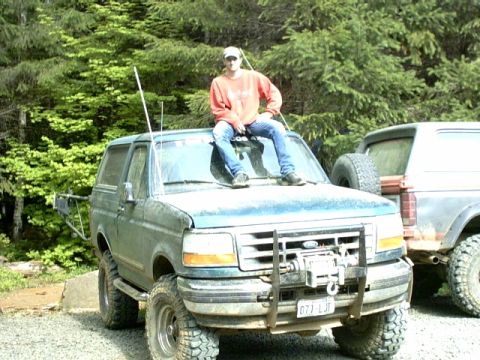 1995 Ford Bronco - A person sits on the hood of a green Ford Bronco, with another Bronco visible behind it.