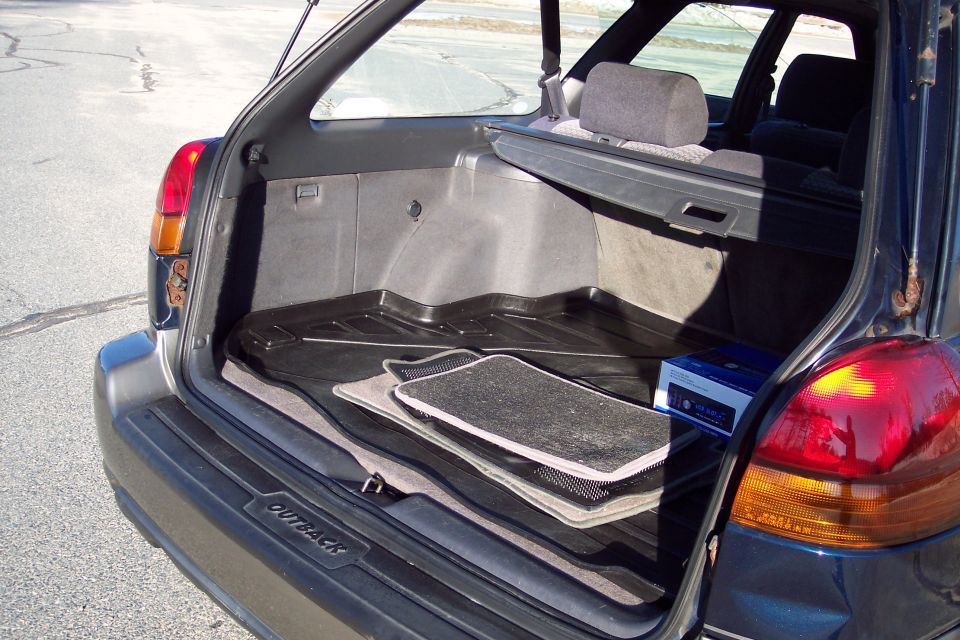 Open trunk of a dark blue Subaru Outback wagon showing cargo liner, mats, and a stereo box.