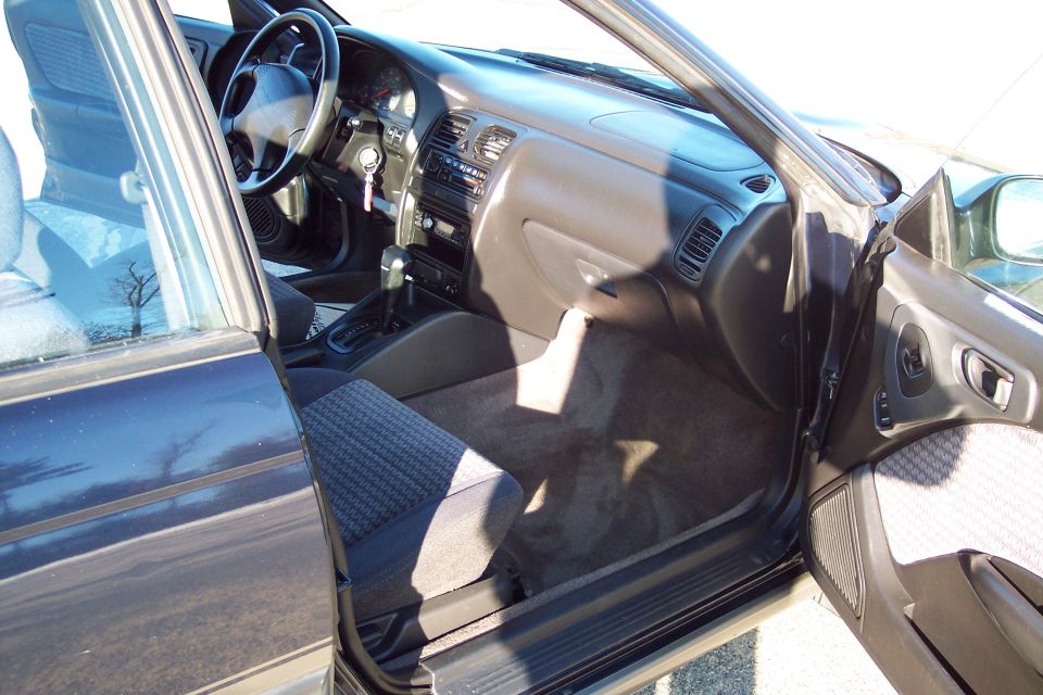 Interior of a dark sedan with driver's door open, showing steering wheel, dashboard, and seats.
