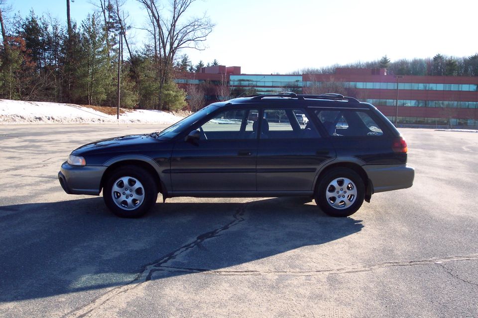 Dark blue and grey Subaru Outback station wagon parked in an asphalt lot.