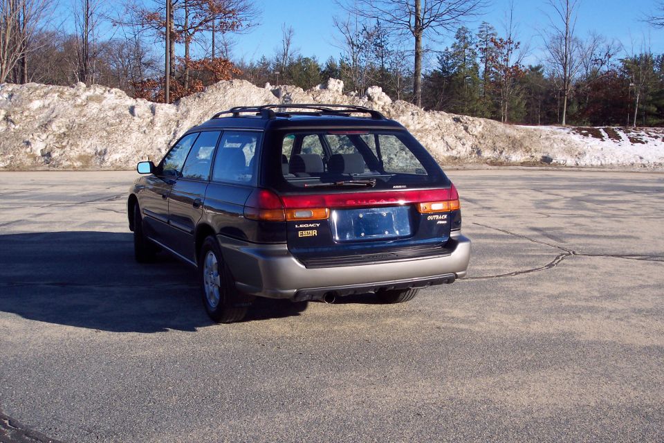 Dark blue Subaru Outback wagon, rear passenger side view, parked on asphalt with snowbanks.