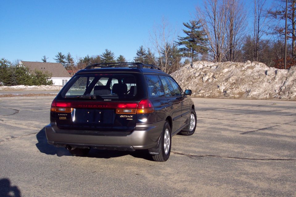 Dark Subaru Outback wagon parked on asphalt lot, rear passenger side view.