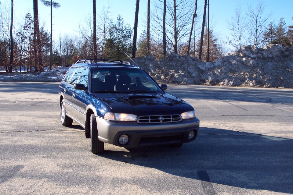 Dark blue Subaru Outback wagon parked outdoors with snow piles and trees in the background.