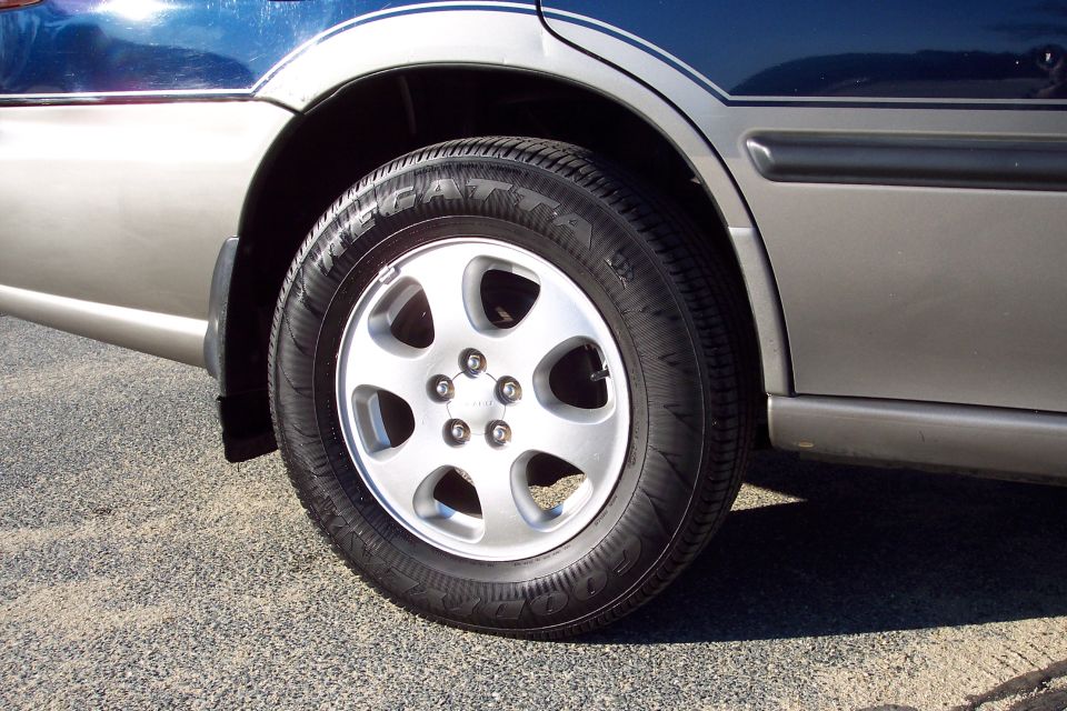 Rear wheel and fender of a dark blue and silver sedan, showing a Goodyear tire and silver alloy wheel.