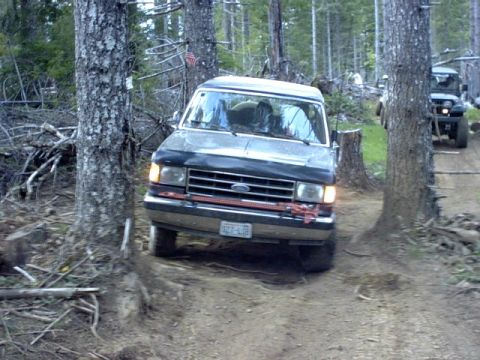 1995 Ford Bronco - A 1995 Ford Bronco navigates a wooded trail, with another vehicle visible in the background.