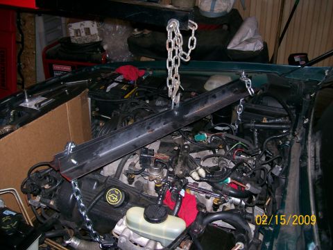 1995 Mercury Grand Marquis - An engine bay is shown with an engine hoist and chains supporting the engine. Various engine components, wiring, and a cardboard box are vi…