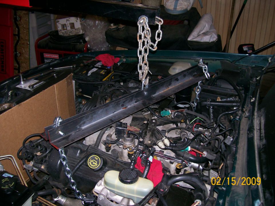 Engine bay with engine hoist and chains, visible engine components and wiring.