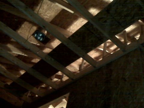 2005 Ford Mustang - The image shows the interior framing of a building, likely an attic, with wooden beams and oriented strand board (OSB) panels. A dark, circ…