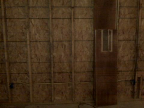 2005 Ford Mustang - A wooden door with a rectangular window is leaning against a wall covered in oriented strand board (OSB) and vertical studs.
