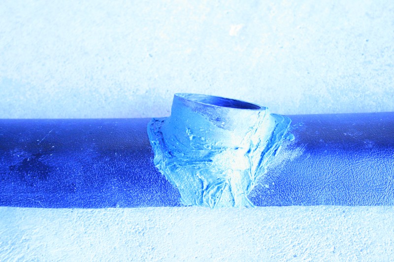 Blue-tinted close-up of a round port with putty on a textured tube
