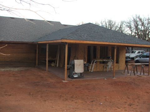 2005 Ford Mustang - A covered patio is under construction next to a wooden house. Construction materials and a grill are visible on the patio, and vehicles are…