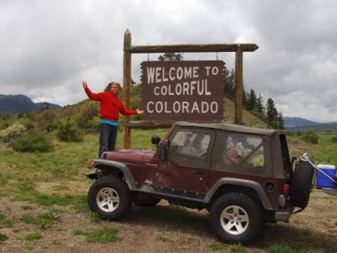 1995 Ford Bronco - A maroon Jeep Wrangler TJ with a black soft top, silver alloy wheels, mud-terrain tires and a rear-mounted spare parked on grass in front o…